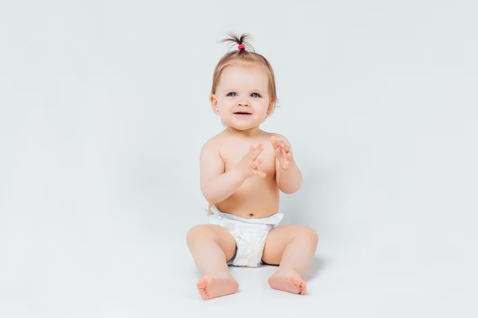 child in a diaper holding hands up and watching on the camera on a white background