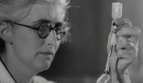woman in glasses holding a vaccine and syringe