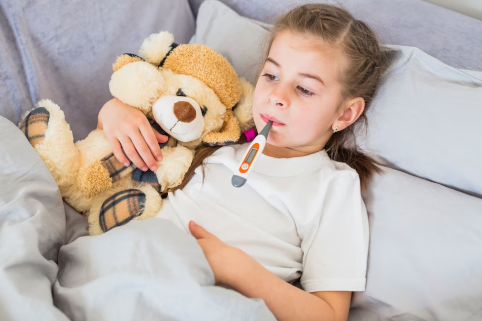 girl with a thermometer in her mouth holding a toy in her bed