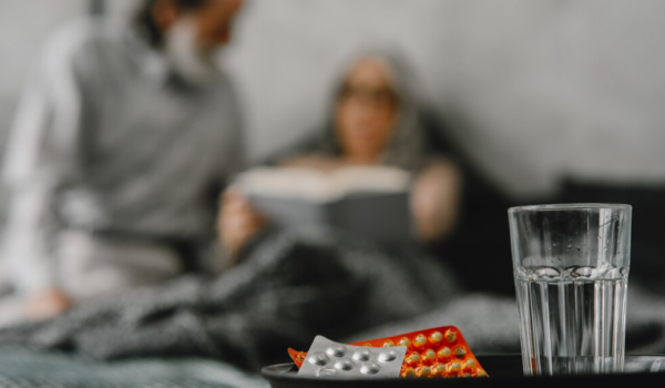 a glass of water, pills, and blurred background of man and woman lying in bed