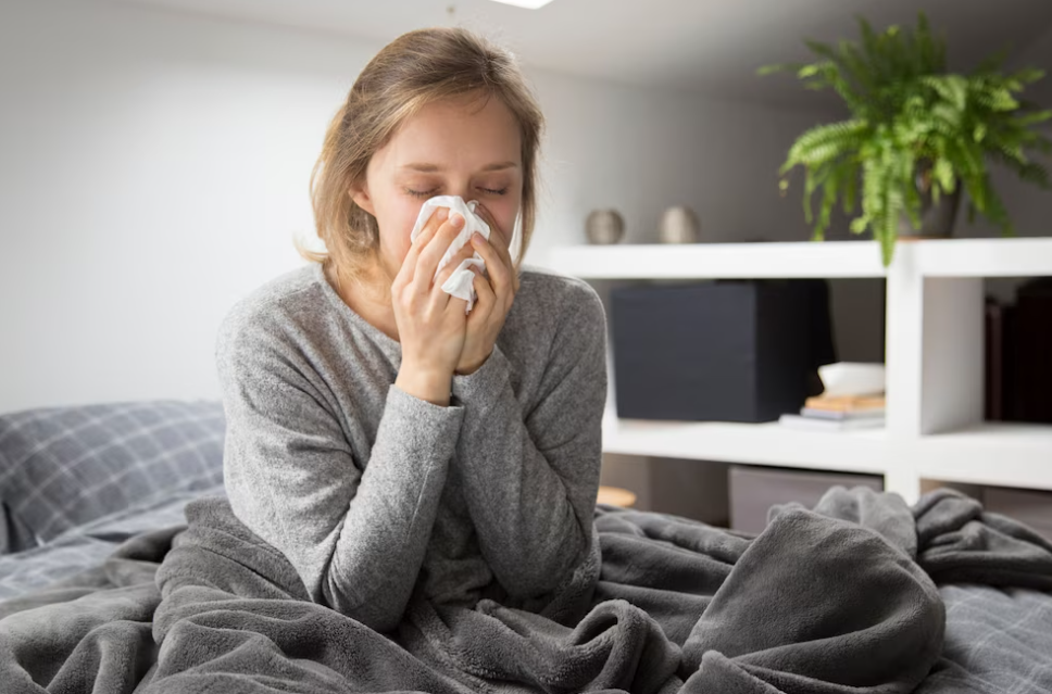 woman in gray sweater sneezing in napkin and sitting in a bed