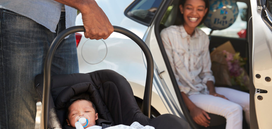 a man holding a baby car seat with a newborn next to a smiling woman in a car