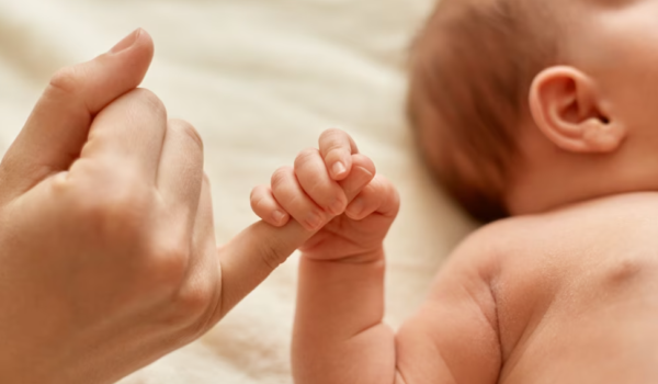 naked infant holding mommy's finger on the bed