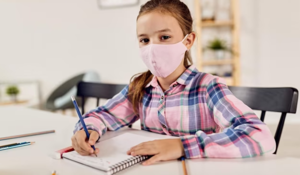 A girl sits in school wearing a mask