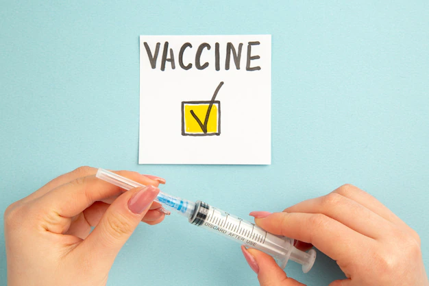 Top view of a note with the inscription vaccine, next to the hands in which the syringe