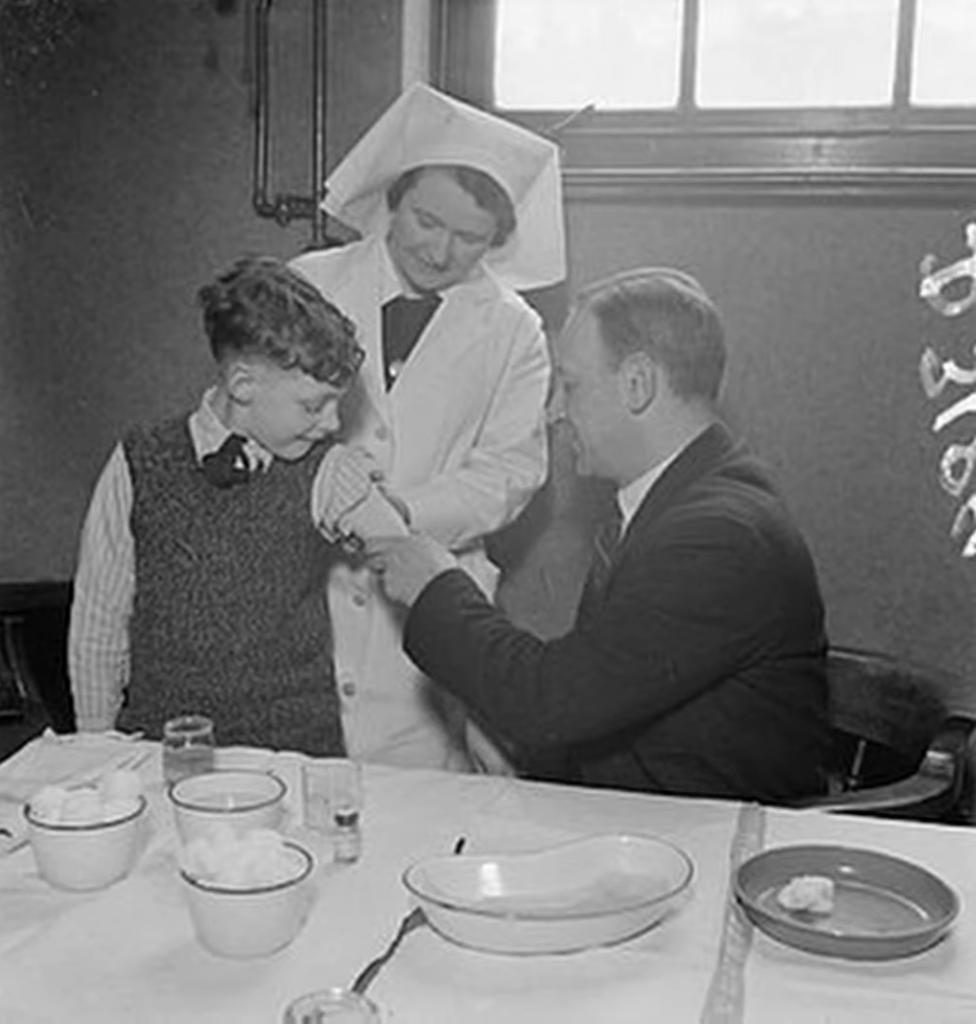 black and white photo of man holding child’s hand, nurse standing near them